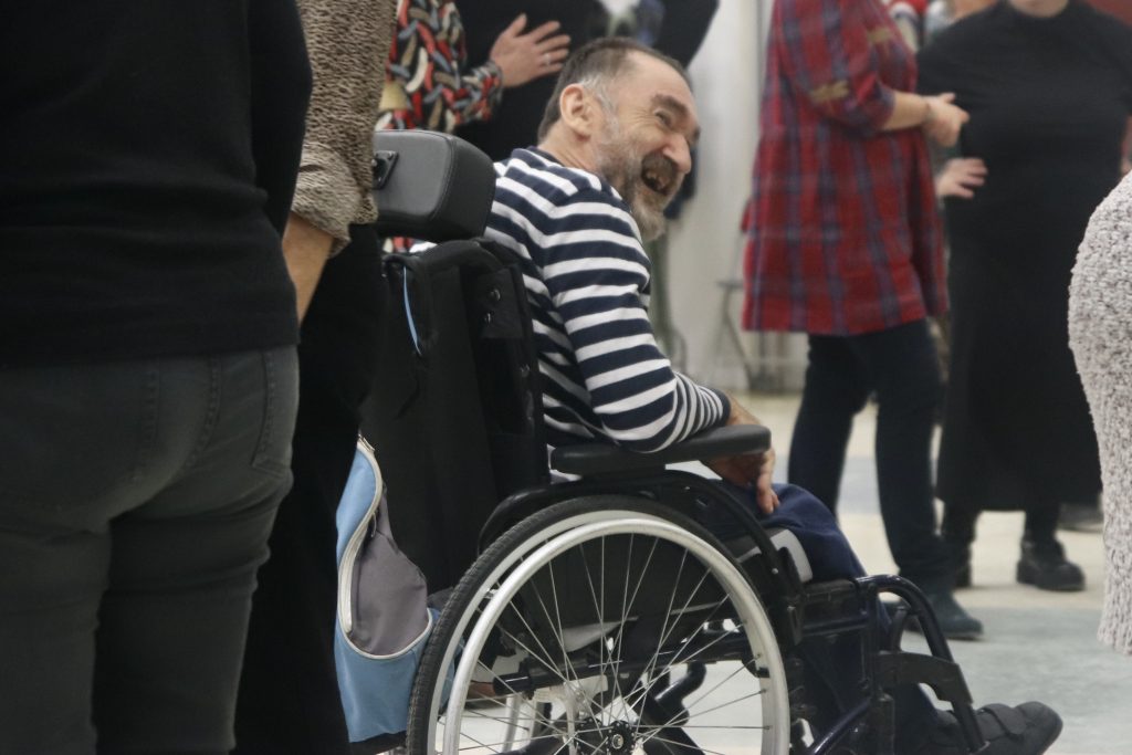 Un monsieur en fauteuil roulant danse et sourit à ses partenaires