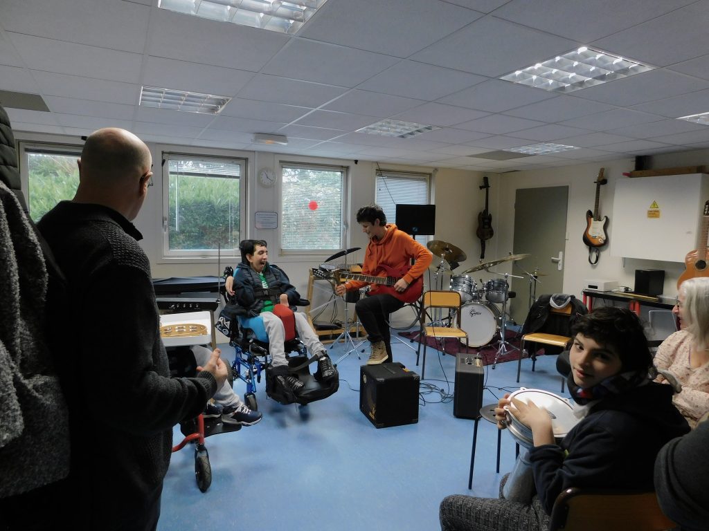 Le groupe complet, avec Clémentine qui montre à un des participants comment jouer de la guitare, et une participante au premier plan qui joue de la percussion